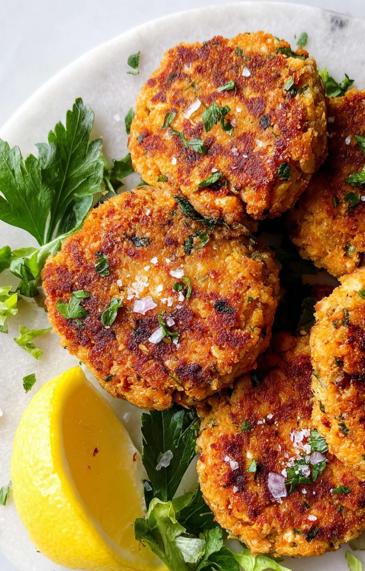 Three air fryer salmon patties sprinkled with sea salt and fresh herbs, served alongside a bright lemon wedge.