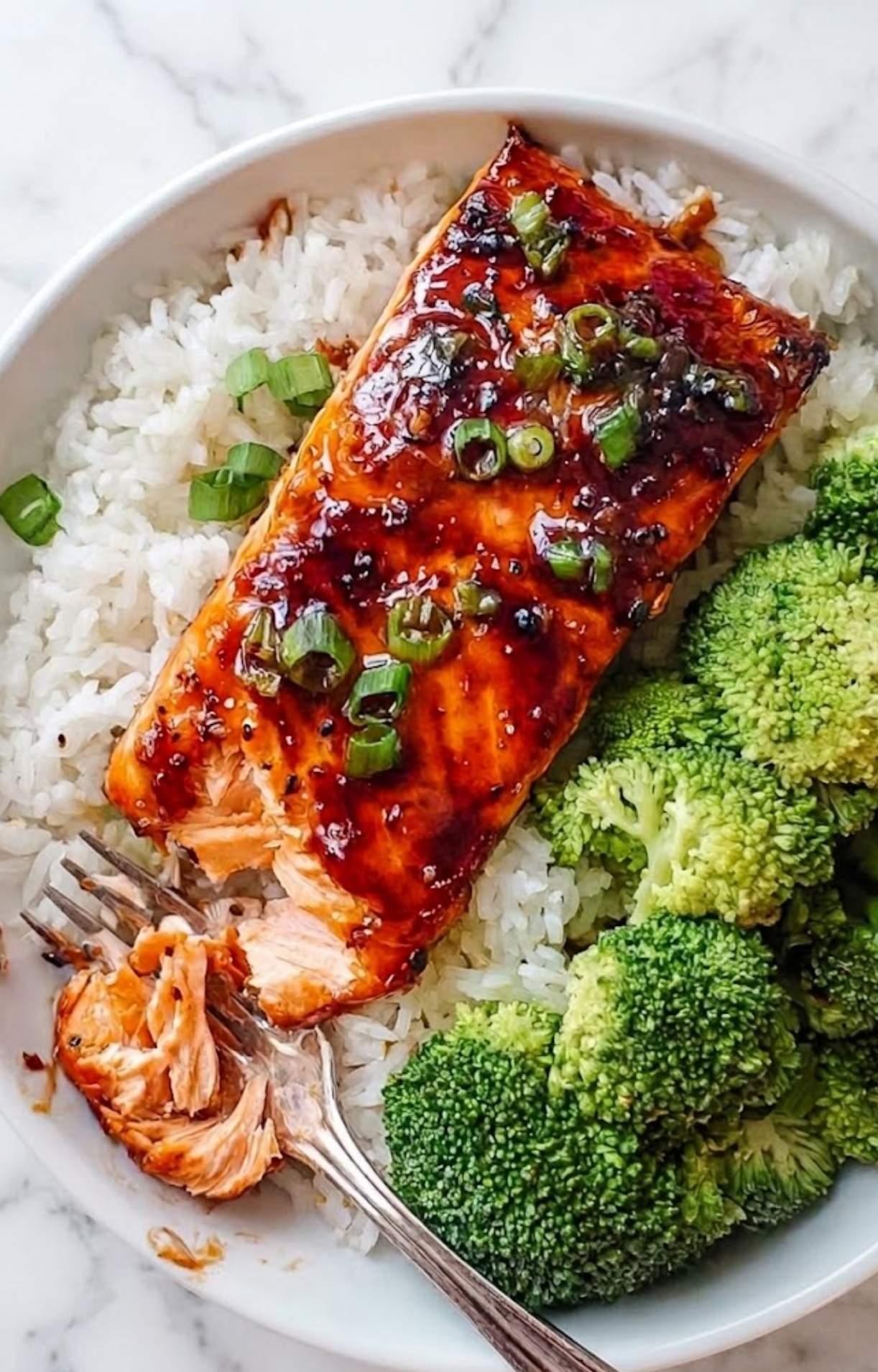 A close-up of a cooked honey garlic salmon fillet being flaked with a fork to show its moist and tender texture.