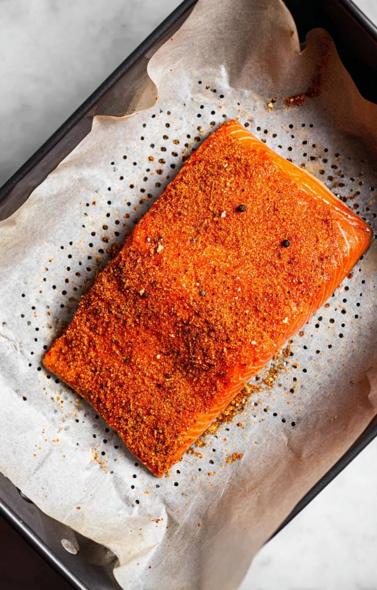 A seasoned salmon fillet placed on a sheet of perforated parchment paper inside an air fryer basket, ready to be cooked.