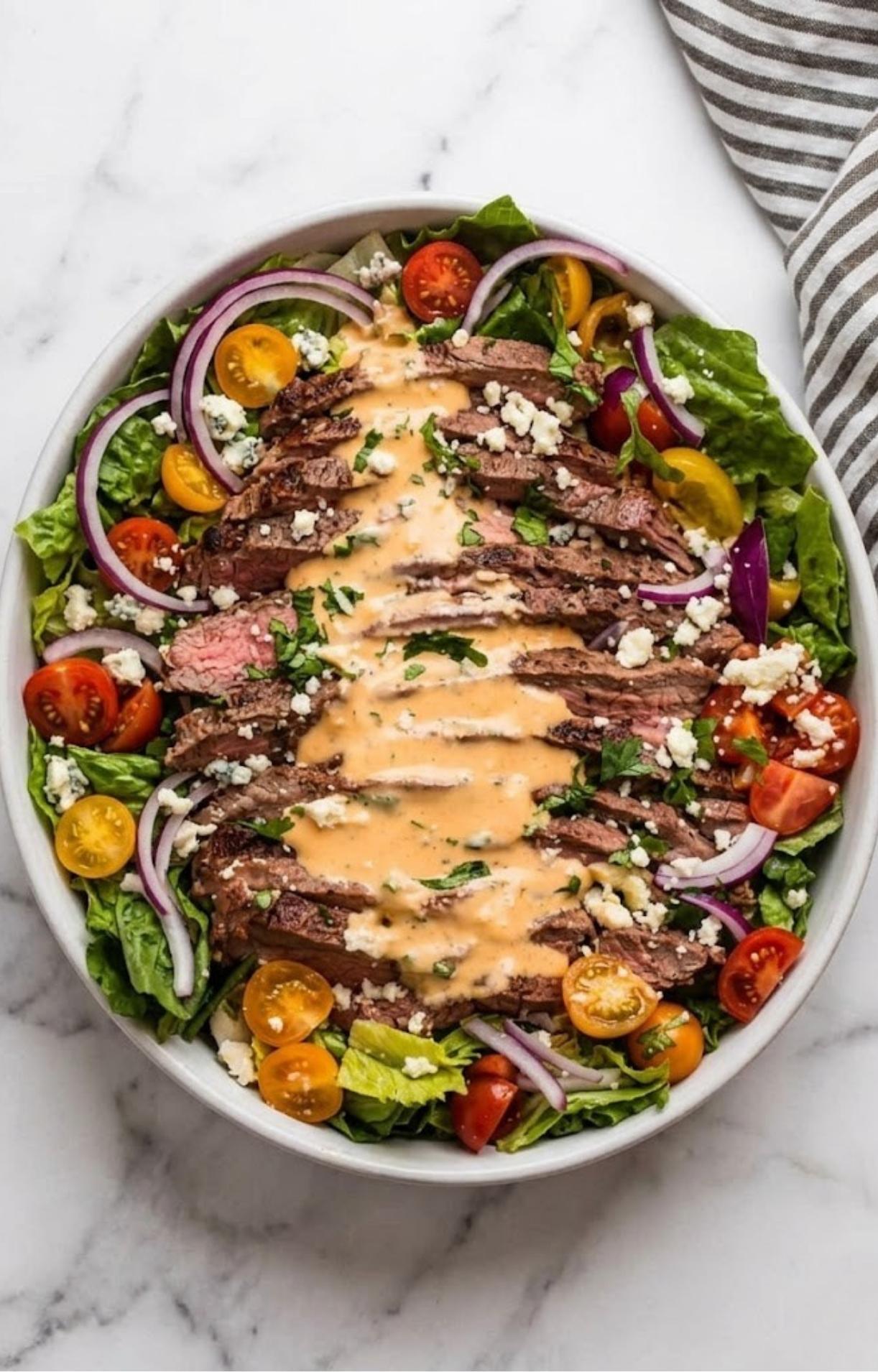 A top-down view of a Flank Steak Salad Recipe being drizzled with a creamy chipotle-style orange dressing.