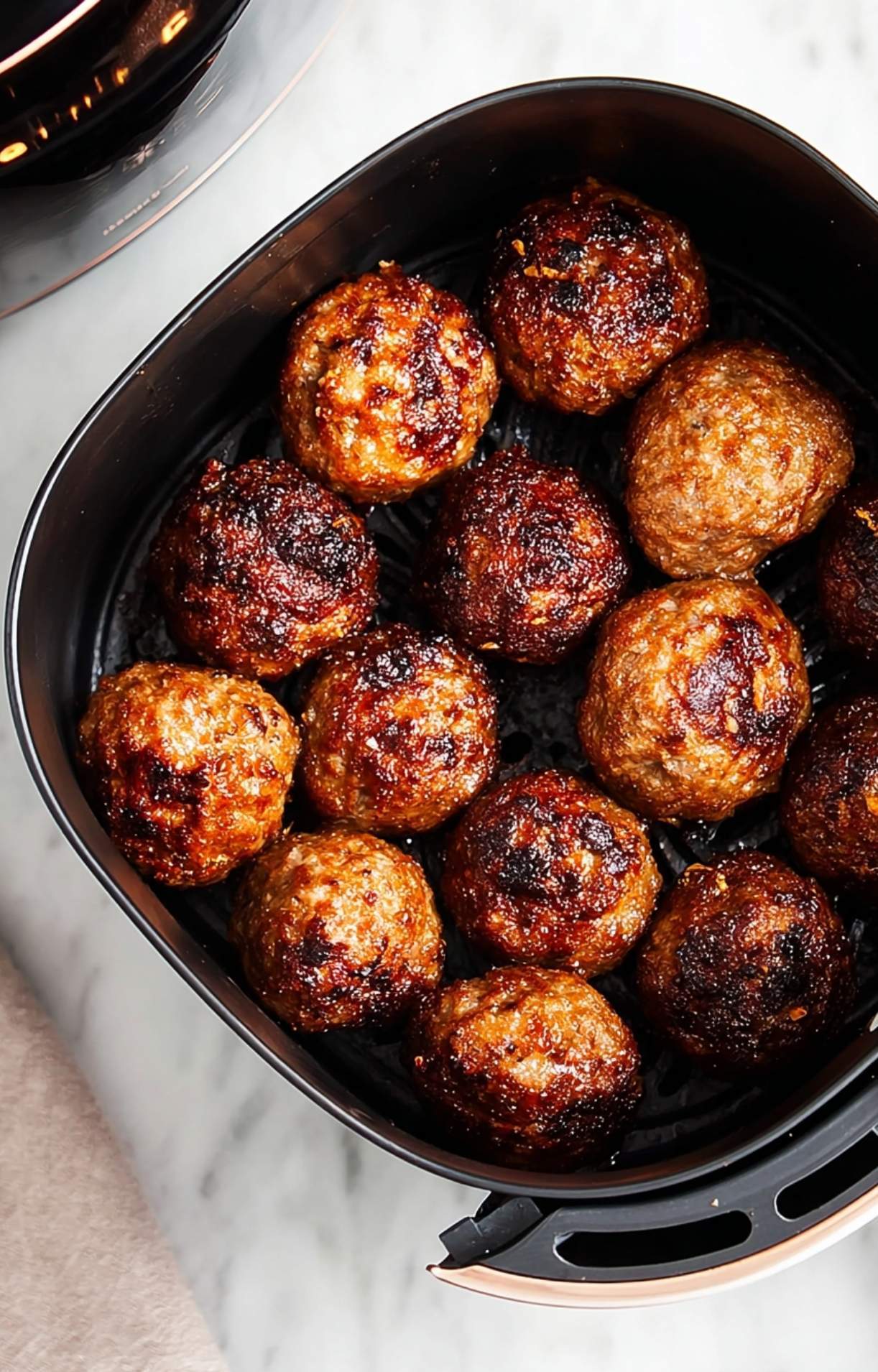 A top-down view of golden-brown chicken meatballs finished cooking inside a black air fryer basket.