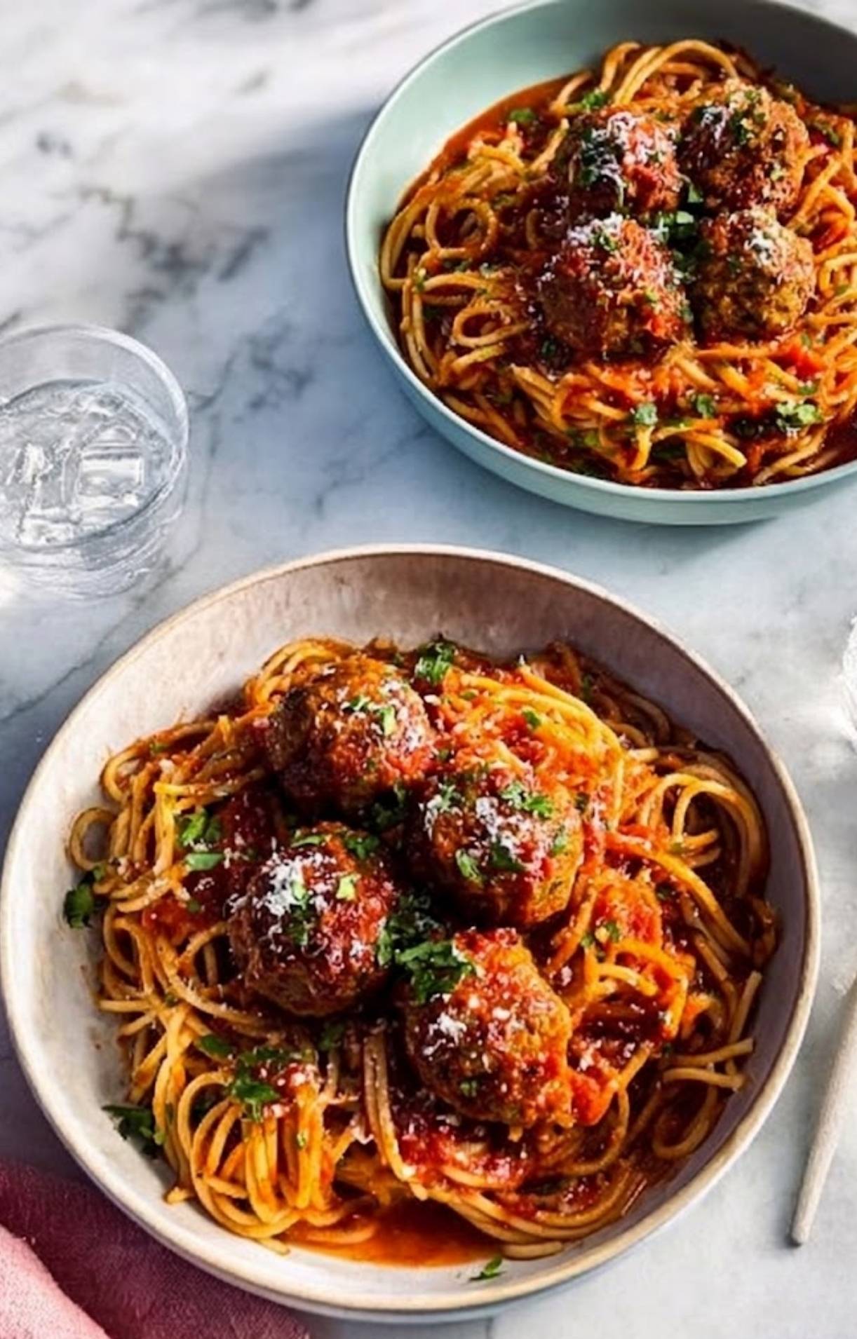 Two bowls of spaghetti and meatballs served on a marble countertop next to a glass of water, perfect for an easy weeknight meal.
