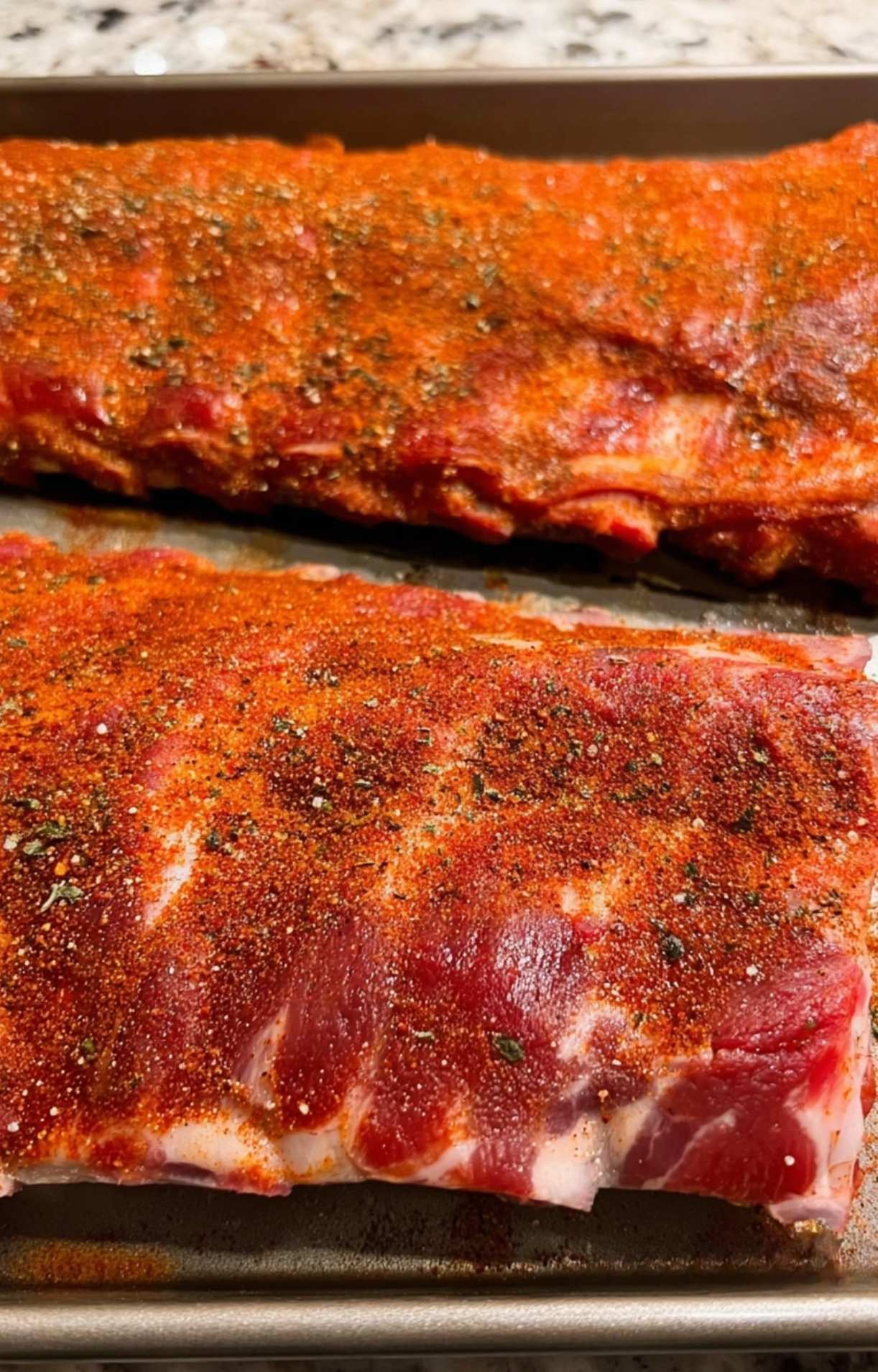 Two racks of raw pork ribs generously coated in a red spice blend for a Pellet Smoker Ribs Recipe.