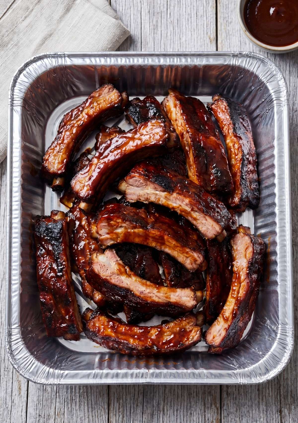 Glazed individual ribs organized in a silver foil baking pan, ready for the final cook.