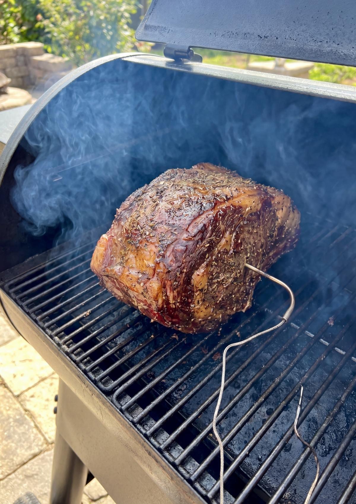 The seasoned standing rib roast placed on the grill grates of a pellet smoker with a meat probe inserted, ready for the smoking process.