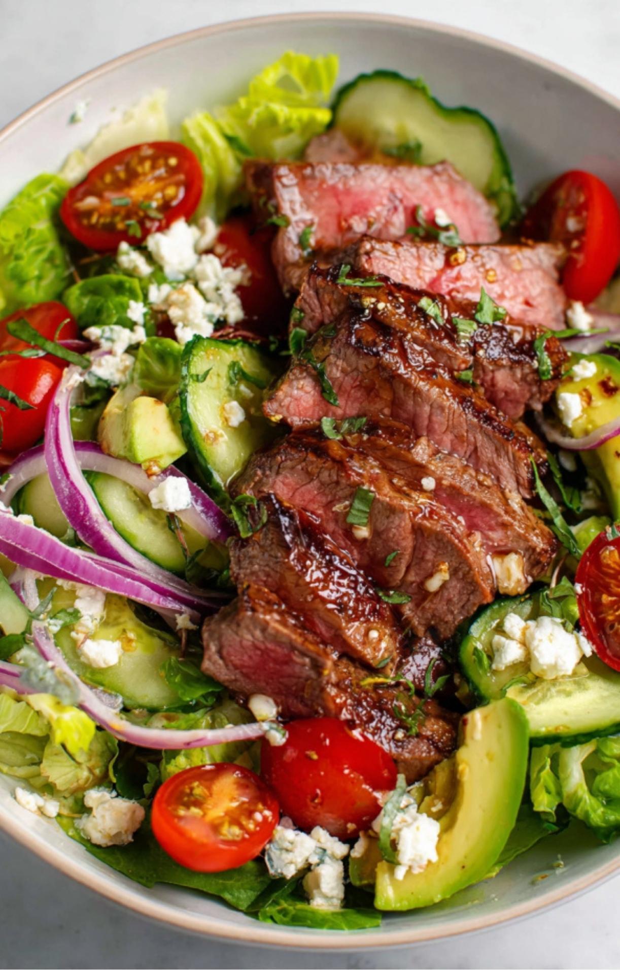 A detailed close-up of a Steak Salad Recipe showcasing the juicy texture of grilled beef slices layered over crisp greens, avocado, and feta cheese.