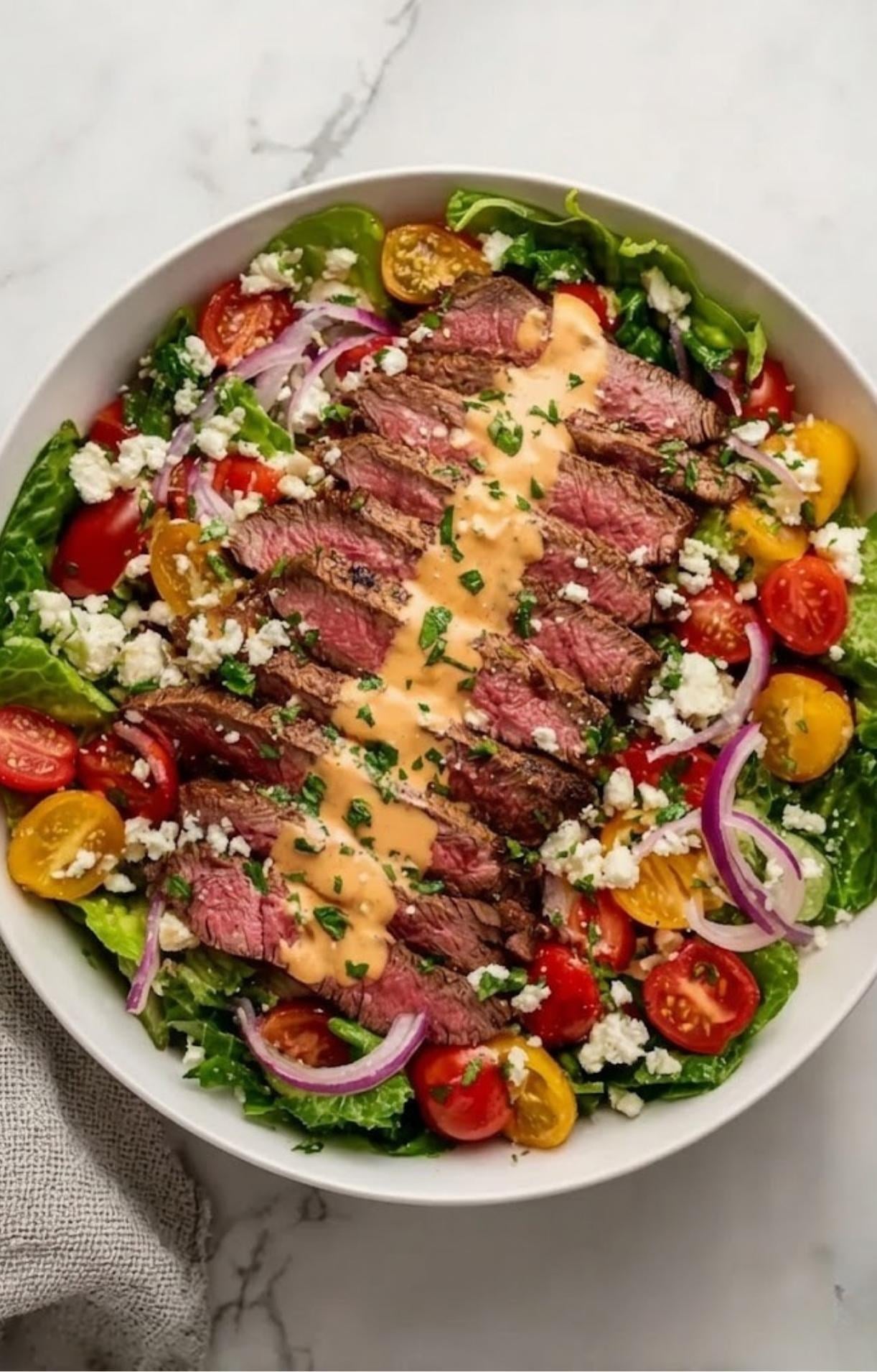 A perfectly assembled Flank Steak Salad Recipe with colorful vegetables, crumbled cheese, and a creamy sauce.