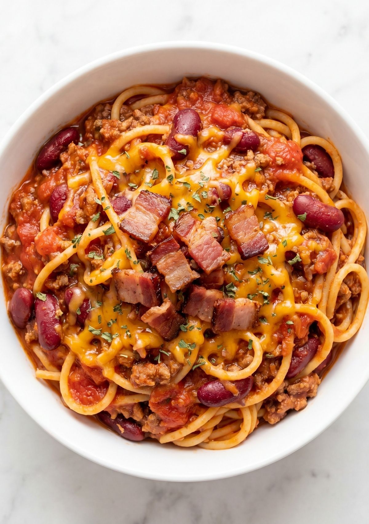 cowboy spaghetti with bacon served in white bowl with beans beef cheese and crispy bacon easy comfort food