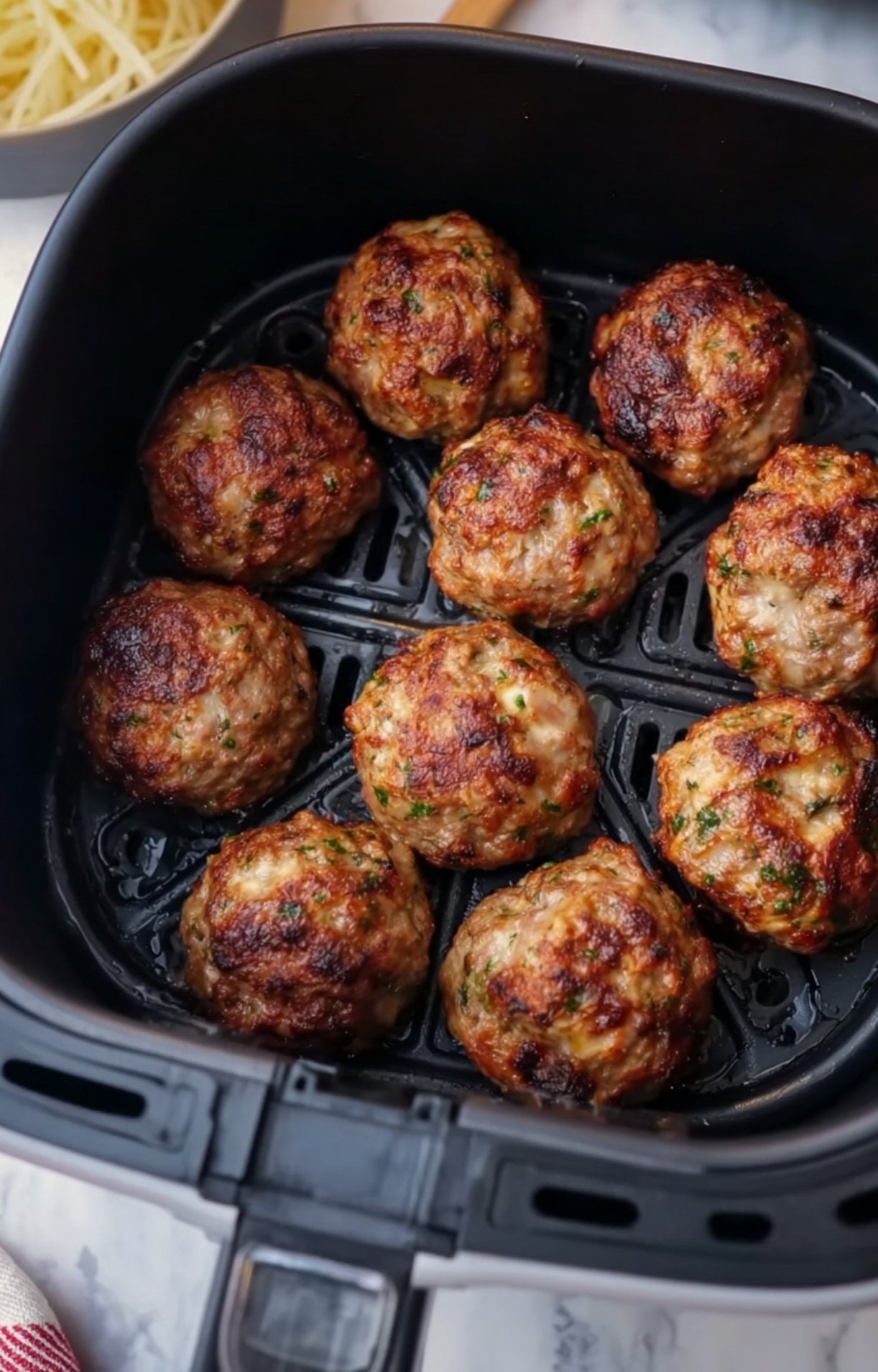 Perfectly cooked, juicy meatballs with a crispy brown exterior sitting in an air fryer basket after cooking.