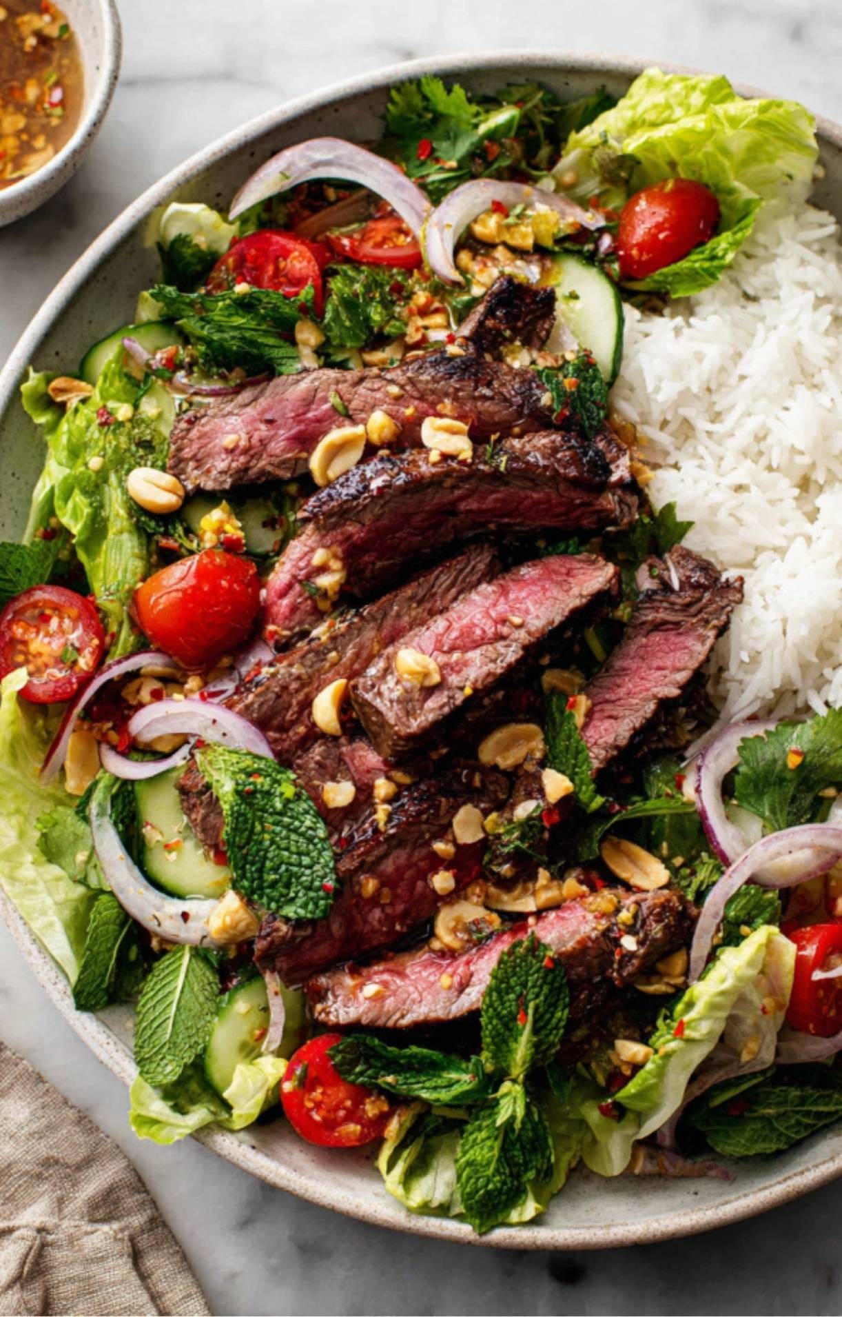 A complete meal featuring juicy steak strips, fresh mint, cucumbers, and red onions served over a bed of rice and lettuce.