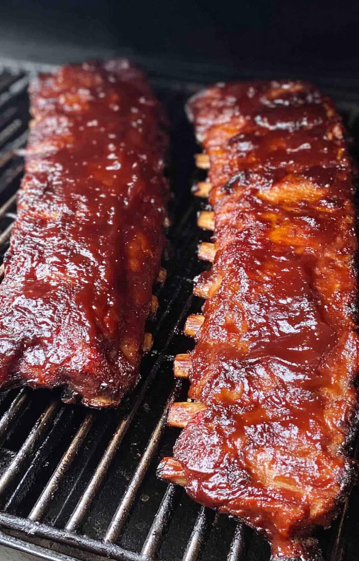 Baby back ribs being glazed with glossy BBQ sauce while cooking on the pellet smoker.