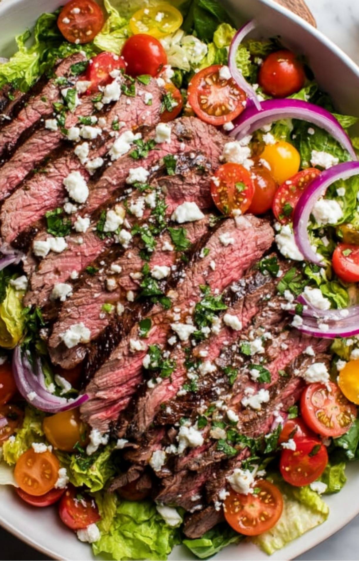 Freshly sliced steak layered over romaine lettuce, cherry tomatoes, and red onions for a Flank Steak Salad Recipe.