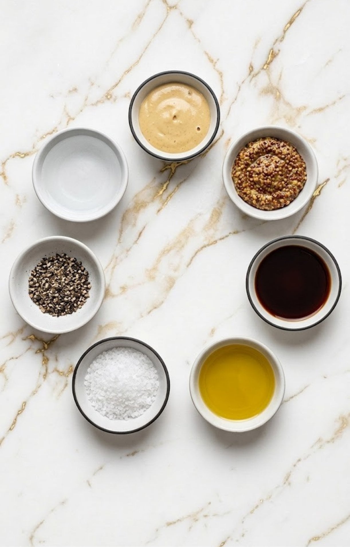 An organized bird's-eye view of small white bowls containing oil, vinegar, two types of mustard, salt, pepper, and water.
