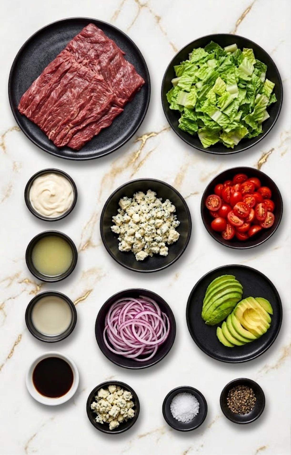 A flat-lay arrangement of ingredients for a Steak and Blue Cheese Salad on a white marble surface, featuring raw sliced steak, chopped romaine lettuce, cherry tomatoes, sliced avocado, red onion rings, blue cheese crumbles, and small bowls containing dressing components like mayonnaise, lemon juice, oil, balsamic glaze, salt, and cracked black pepper.