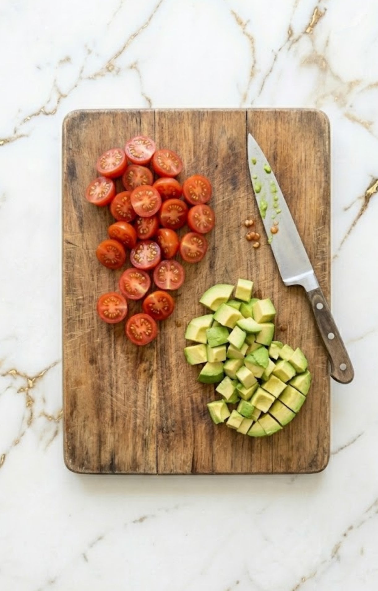 A wooden cutting board showing halved cherry tomatoes and diced avocado cubes being prepared for an Easy Steak Taco Salad Recipe.