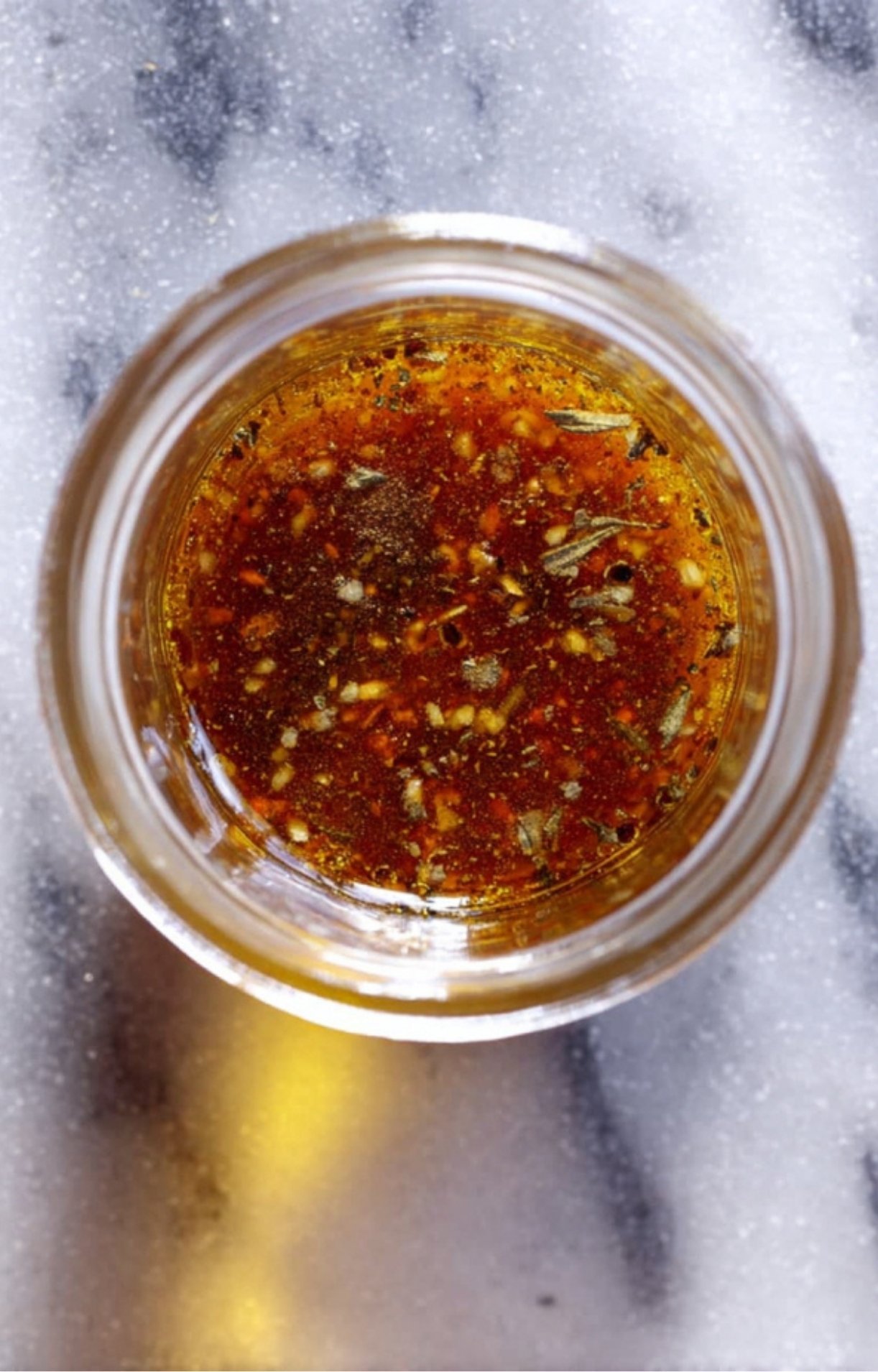 A top-down view of a small glass jar containing a dark, herb-infused balsamic dressing or marinade for a Steak Salad Recipe.