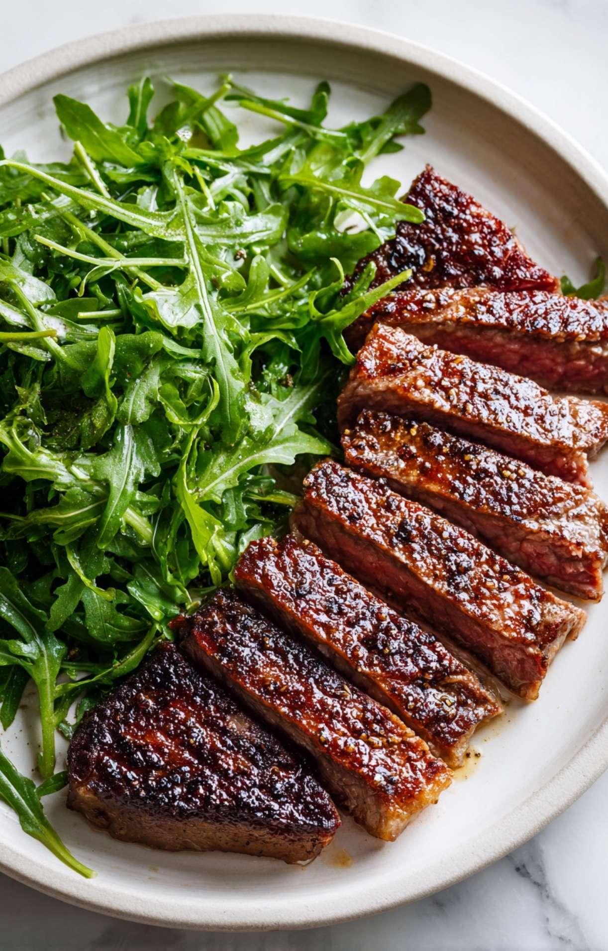 A high-angle detail shot of the beautifully crusted steak slices and dressed arugula salad, emphasizing the textures of the meal.