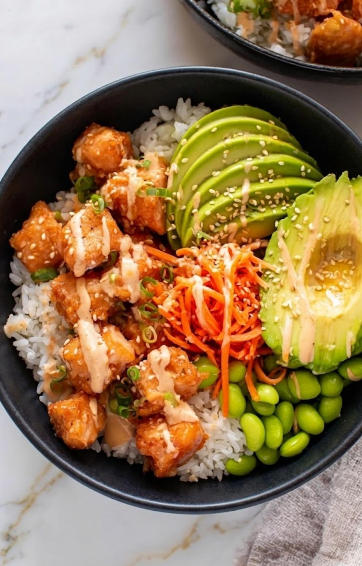 A top-down close-up showing the artistic arrangement of avocado slices, carrots, and edamame alongside salmon in an Air Fryer Salmon Bowl.