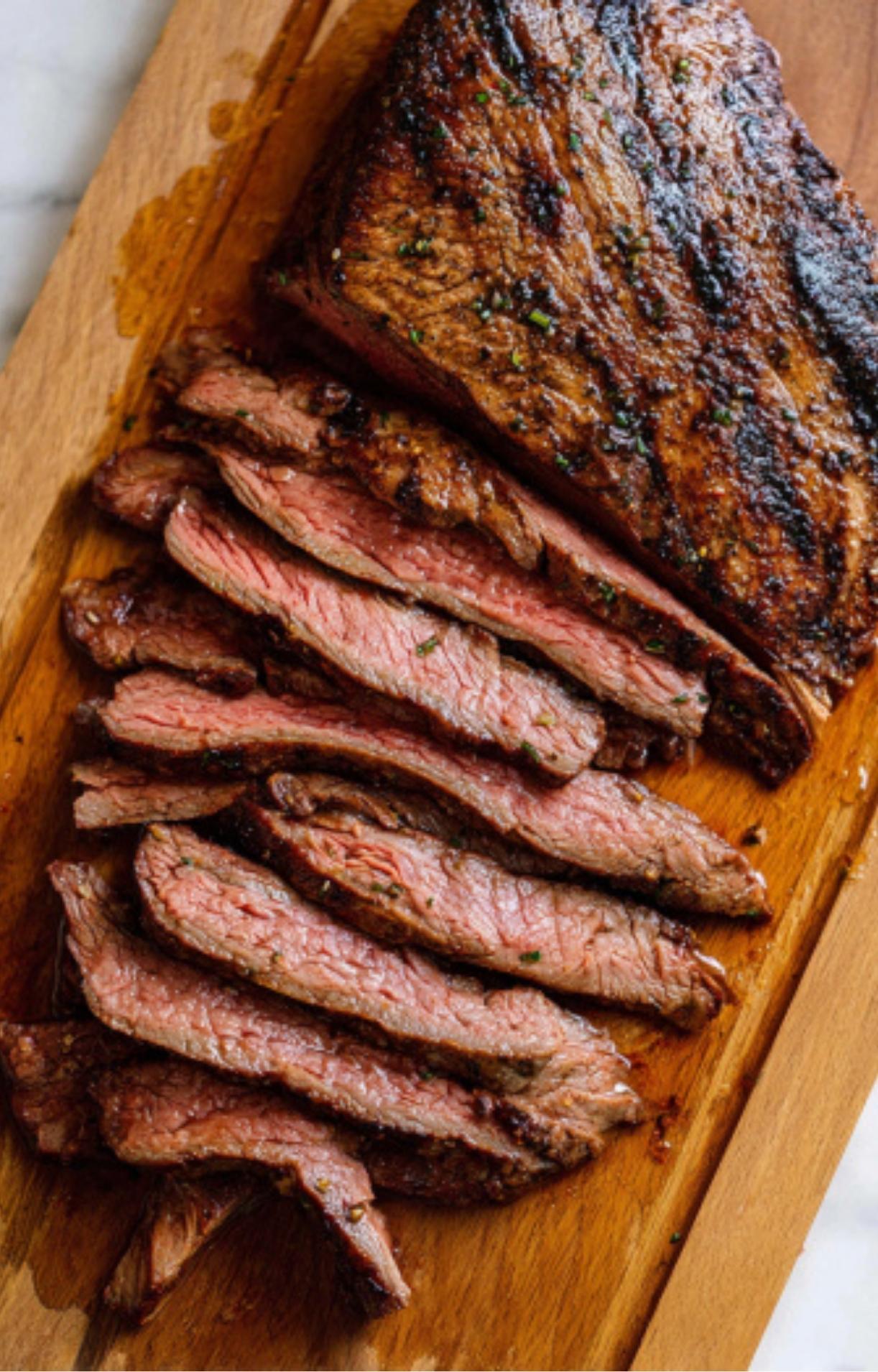 Thin, tender slices of grilled beef on a wooden board, a key step for a Flank Steak Salad Recipe.