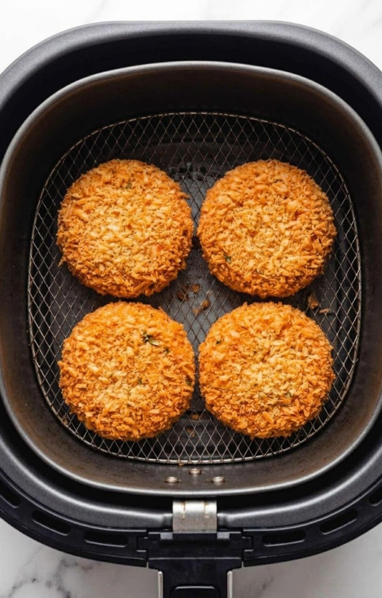 Four golden-brown salmon patties cooking inside an air fryer basket until perfectly crisp.