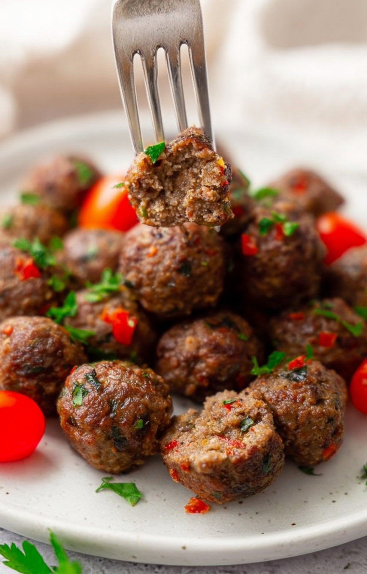 A silver fork holding a half-eaten lamb kofta meatball to reveal the tender, well-seasoned interior with bits of red pepper and herbs.