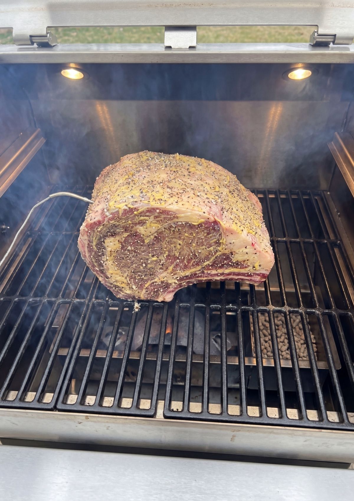 Wisps of blue smoke surround a browning standing rib roast inside a pellet smoker, showing the development of a flavorful crust.