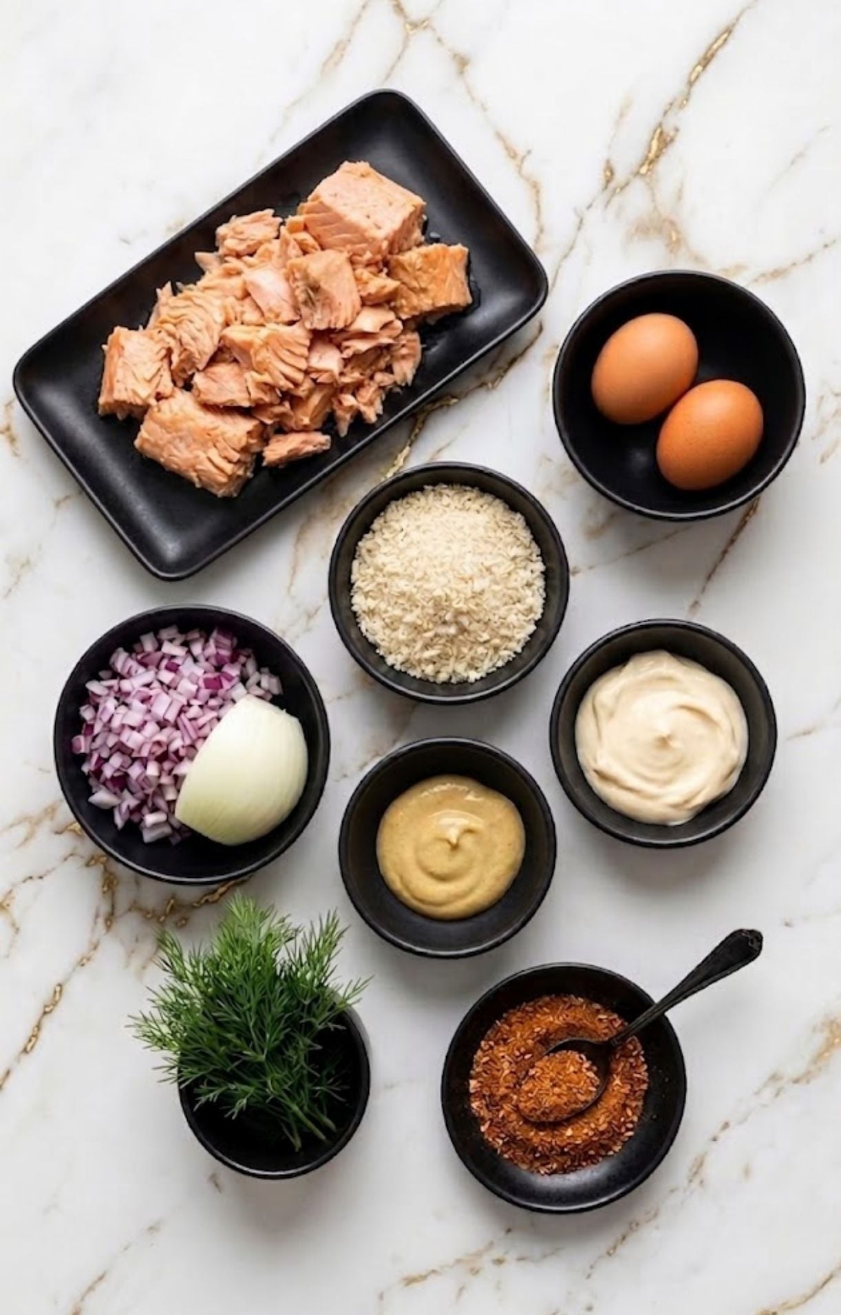 An overhead flat lay of salmon, eggs, breadcrumbs, mayo, mustard, dill, and spices used to make air fryer salmon patties.
