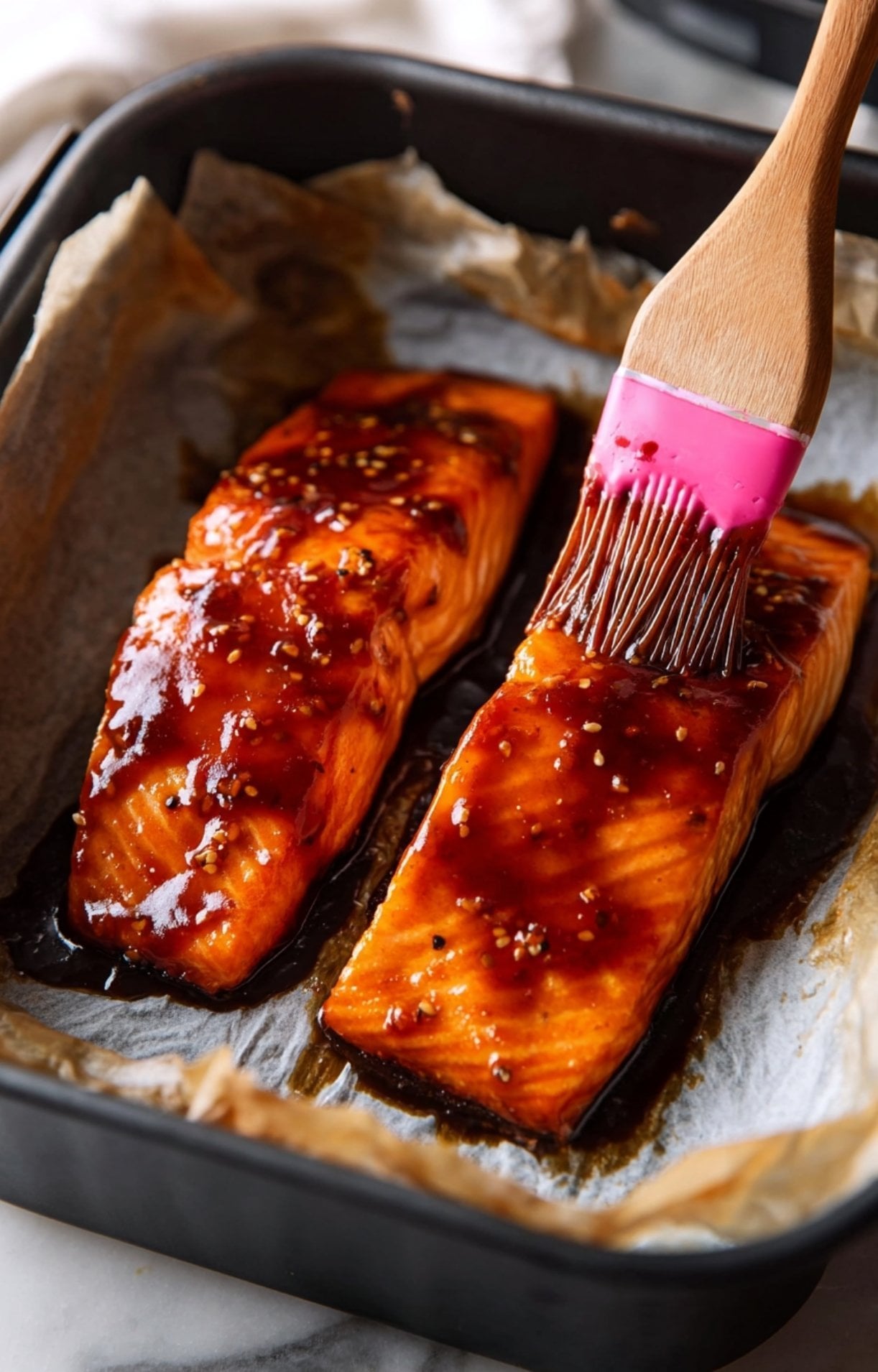Brushing a thick, homemade teriyaki glaze onto raw salmon fillets in an air fryer basket.