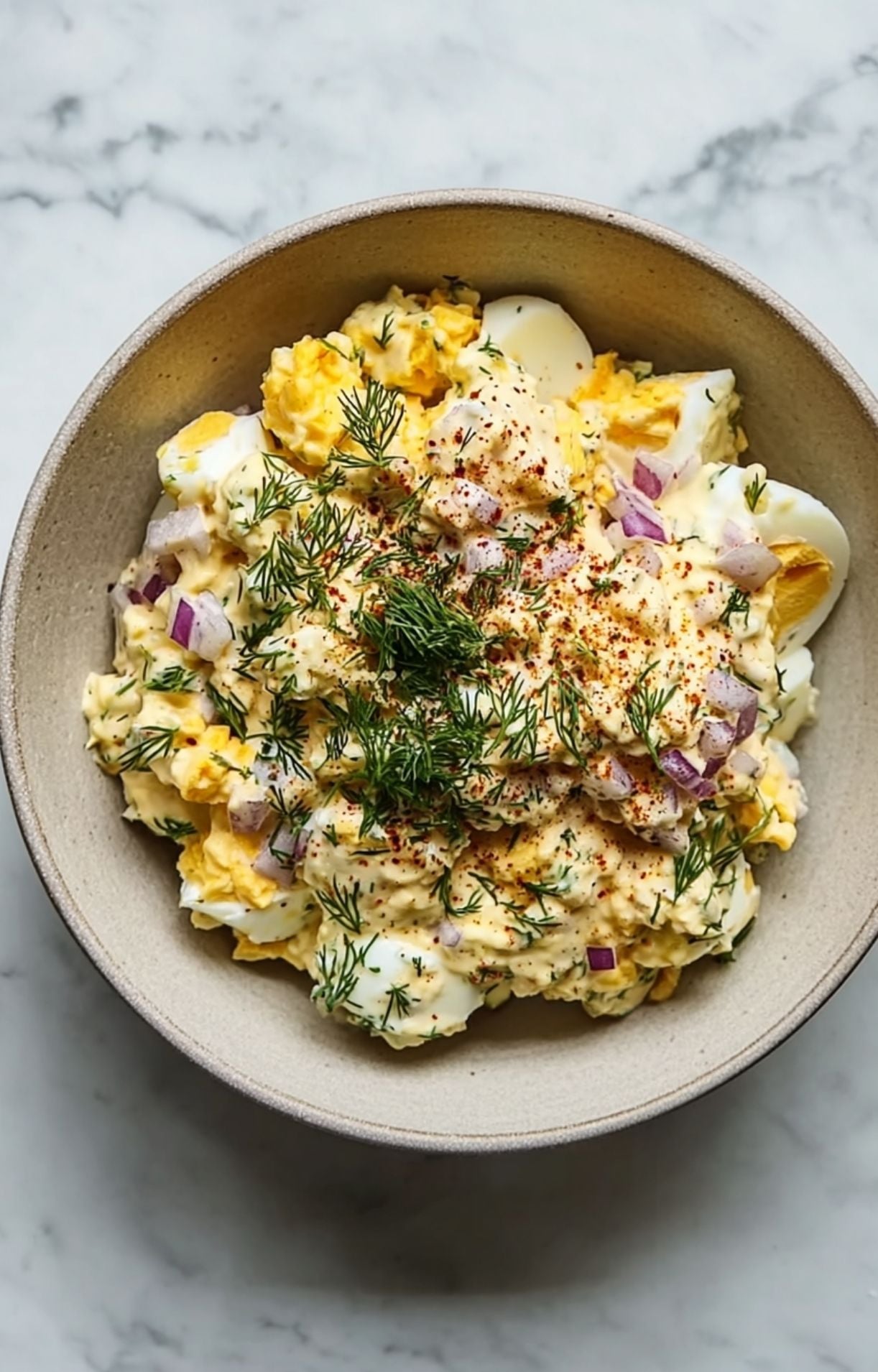 A mixing bowl containing chopped red onions, hard-boiled eggs, fresh dill, and spices being prepped for air fryer salmon patties.