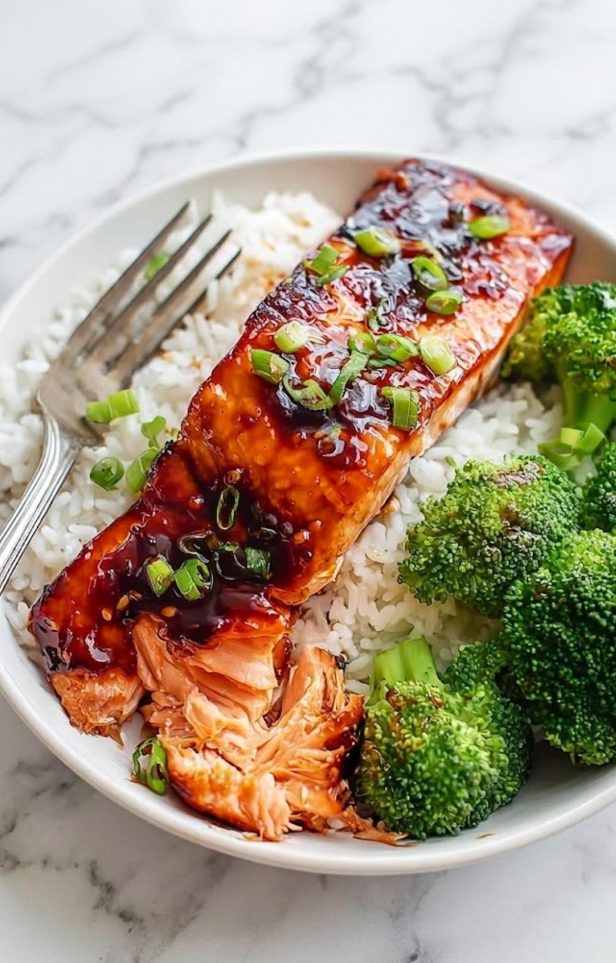 A perfectly glazed honey garlic salmon fillet garnished with fresh sliced green onions and served with broccoli and rice.