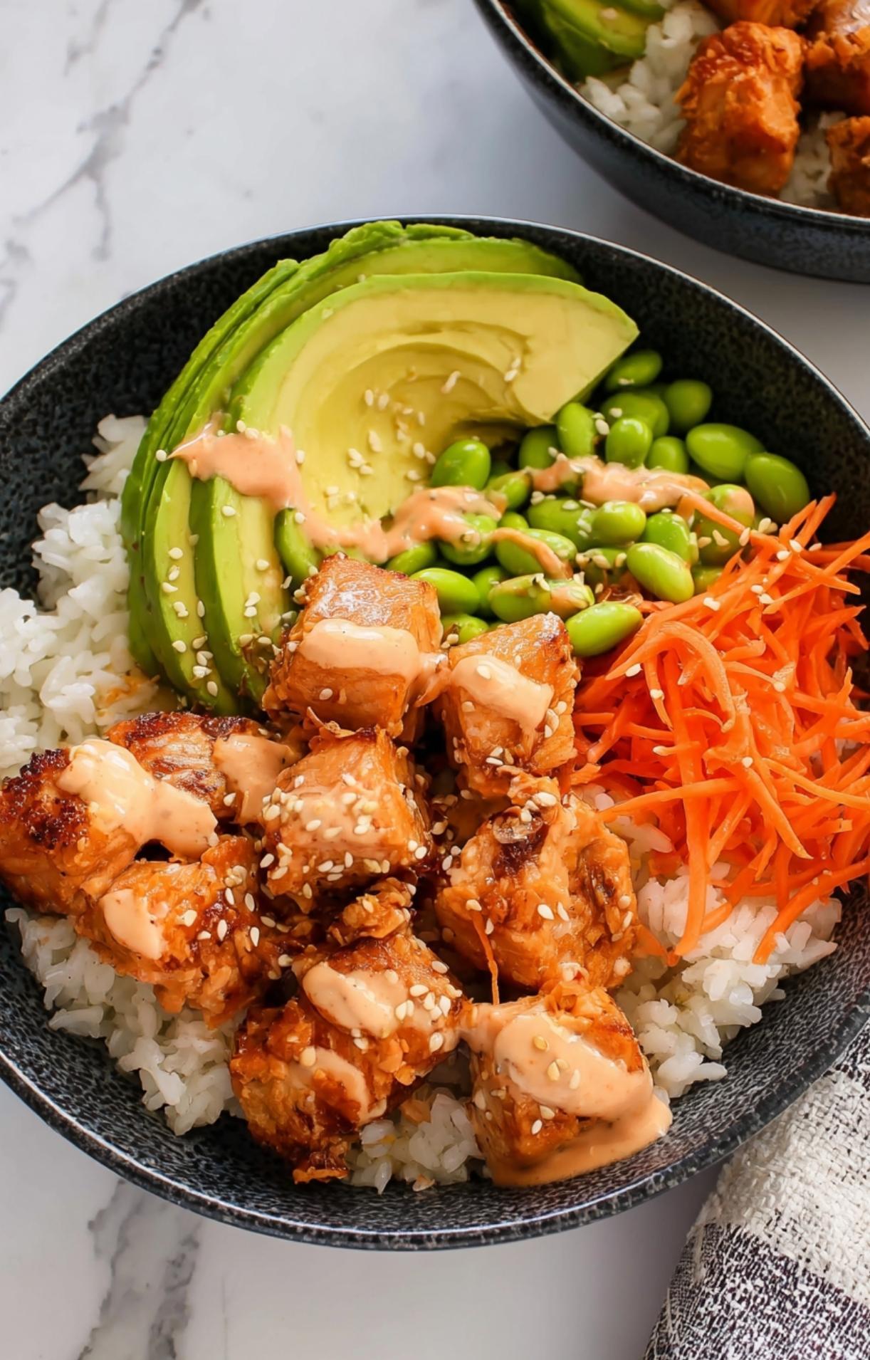 A detailed shot of spicy mayo drizzled over salmon cubes and sesame seeds, highlighting the textures of an Air Fryer Salmon Bowl.