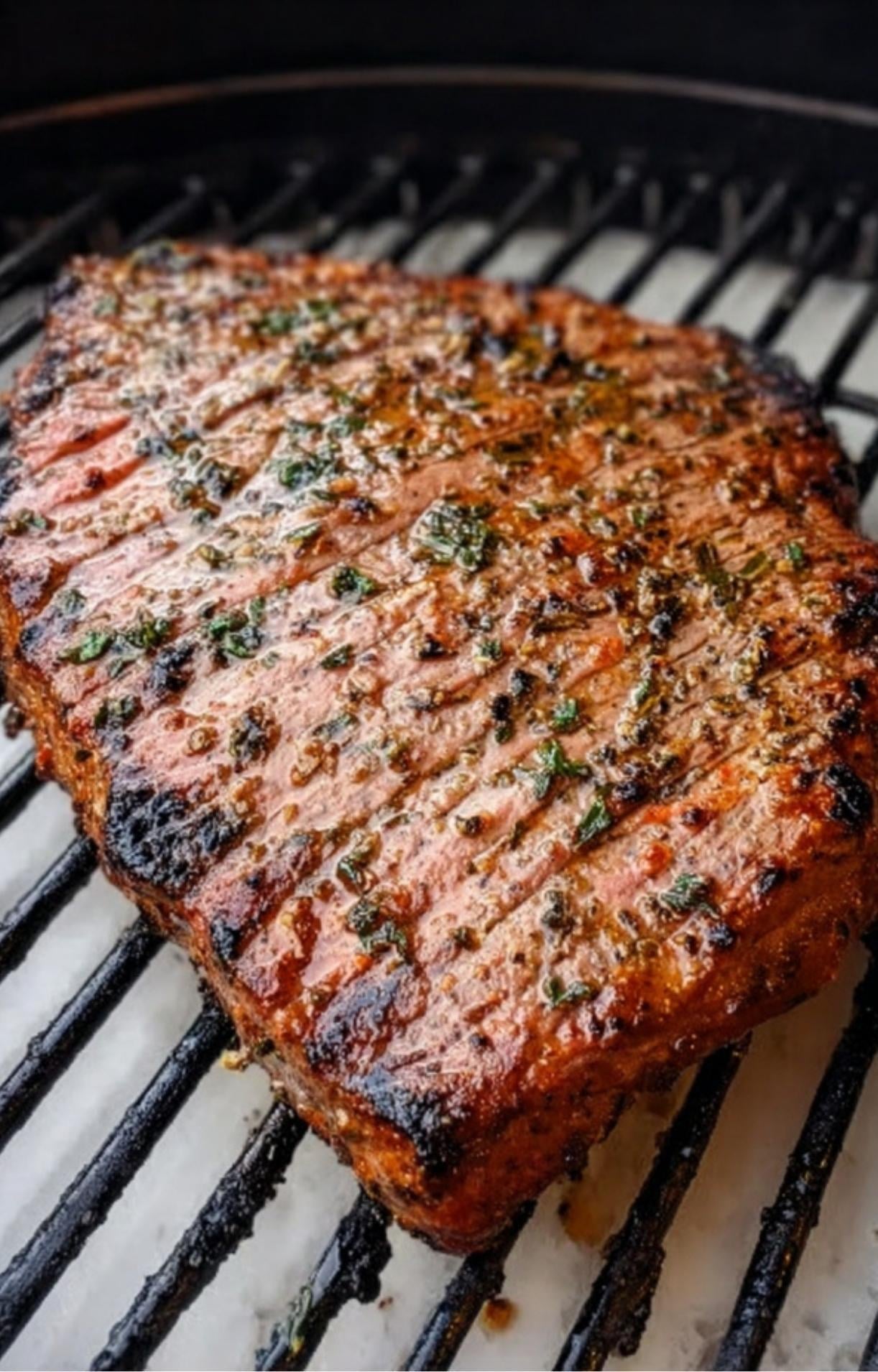 A seasoned flank steak searing on a charcoal grill to create a charred crust for the Flank Steak Salad Recipe.
