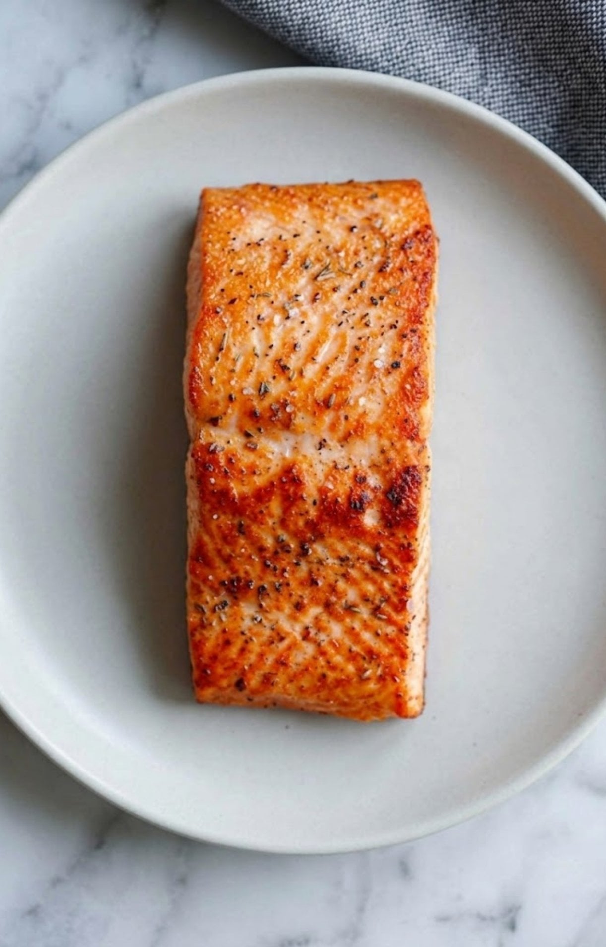 The flesh side of a cooked salmon fillet showing a beautiful golden-orange sear and herb seasoning.