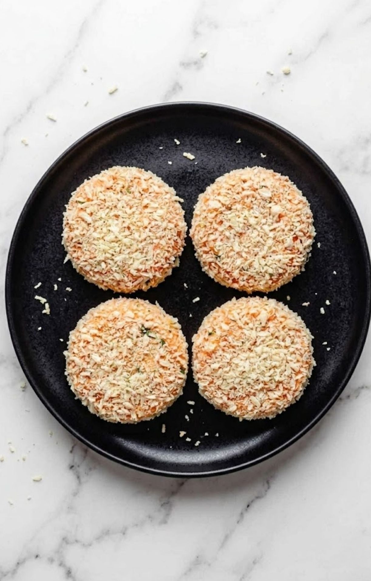 Four breaded salmon patties arranged on a black plate, ready to be cooked in the air fryer.
