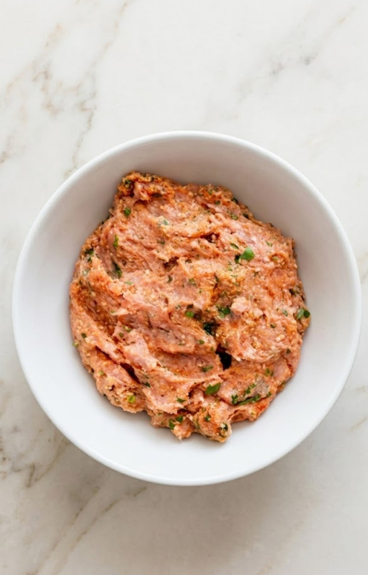 Raw ground turkey meatball mixture thoroughly combined with herbs and spices in a white ceramic bowl.
