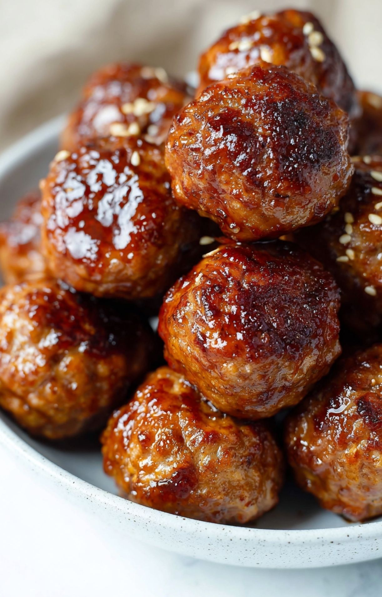 A macro shot of perfectly browned and crispy frozen meatballs air fryer stacked in a light-colored ceramic bowl.