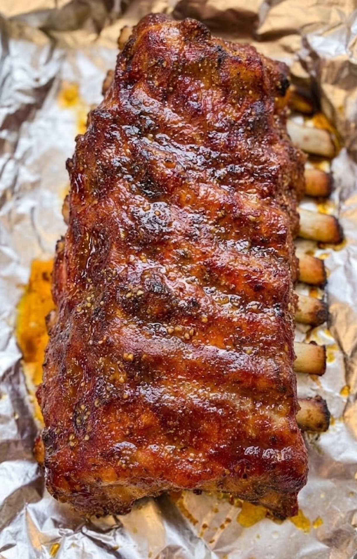 A rack of ribs with a golden-brown bark resting on aluminum foil during the cooking process of a Pellet Smoker Ribs Recipe.