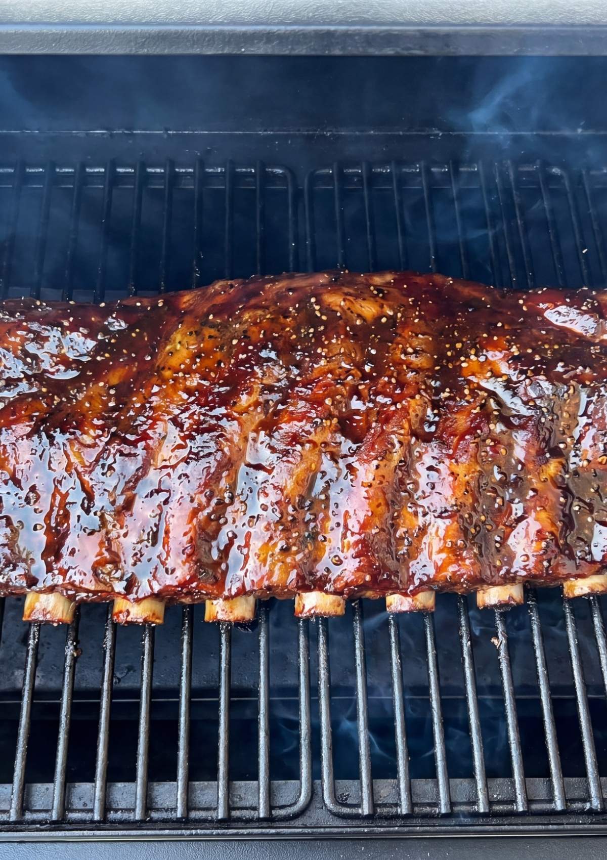 beef ribs pellet smoker recipe with ribs cooking on pellet grill covered in sticky BBQ sauce and smoke