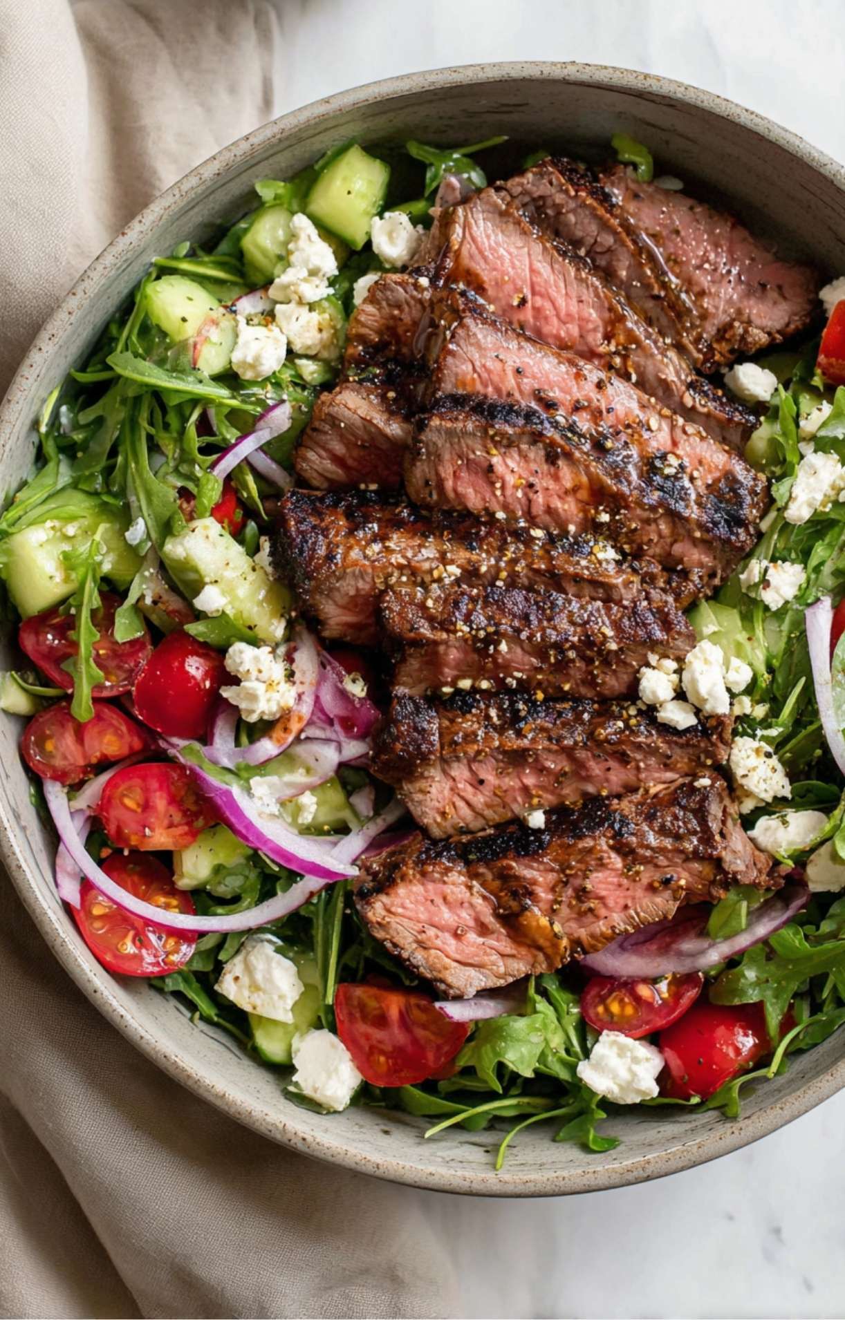 A detailed close-up of a Healthy Steak Salad Recipe showing the charred exterior and pink center of sliced steak topped with cracked black pepper and feta.