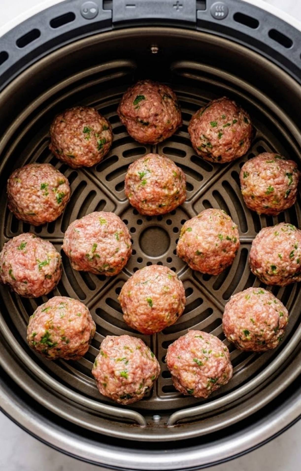 Raw turkey meatballs evenly spaced in a circular pattern inside a black air fryer basket before cooking.