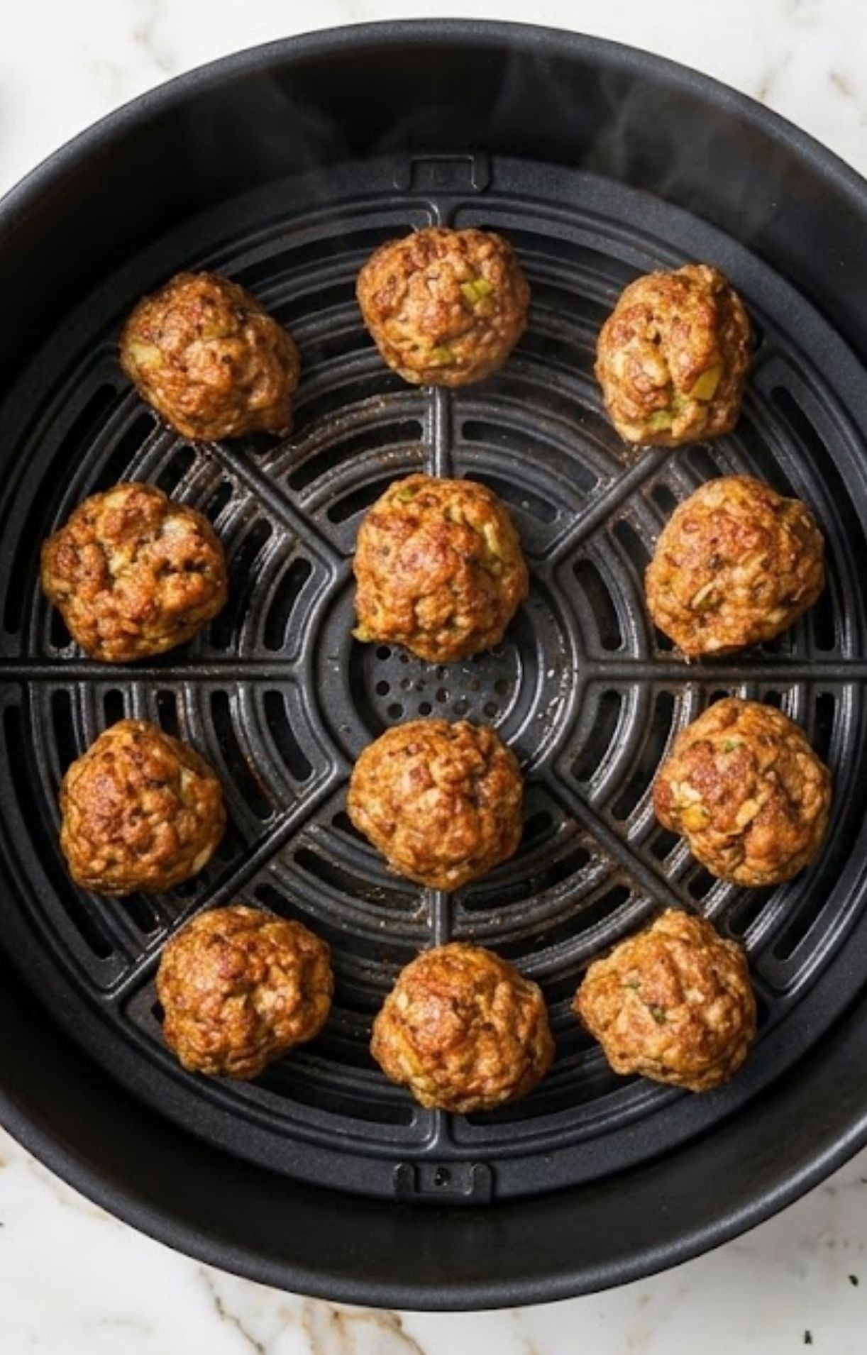 Fully cooked, golden-brown pork meatballs arranged in a circular pattern inside a black air fryer basket, showing a crispy exterior and steam rising.