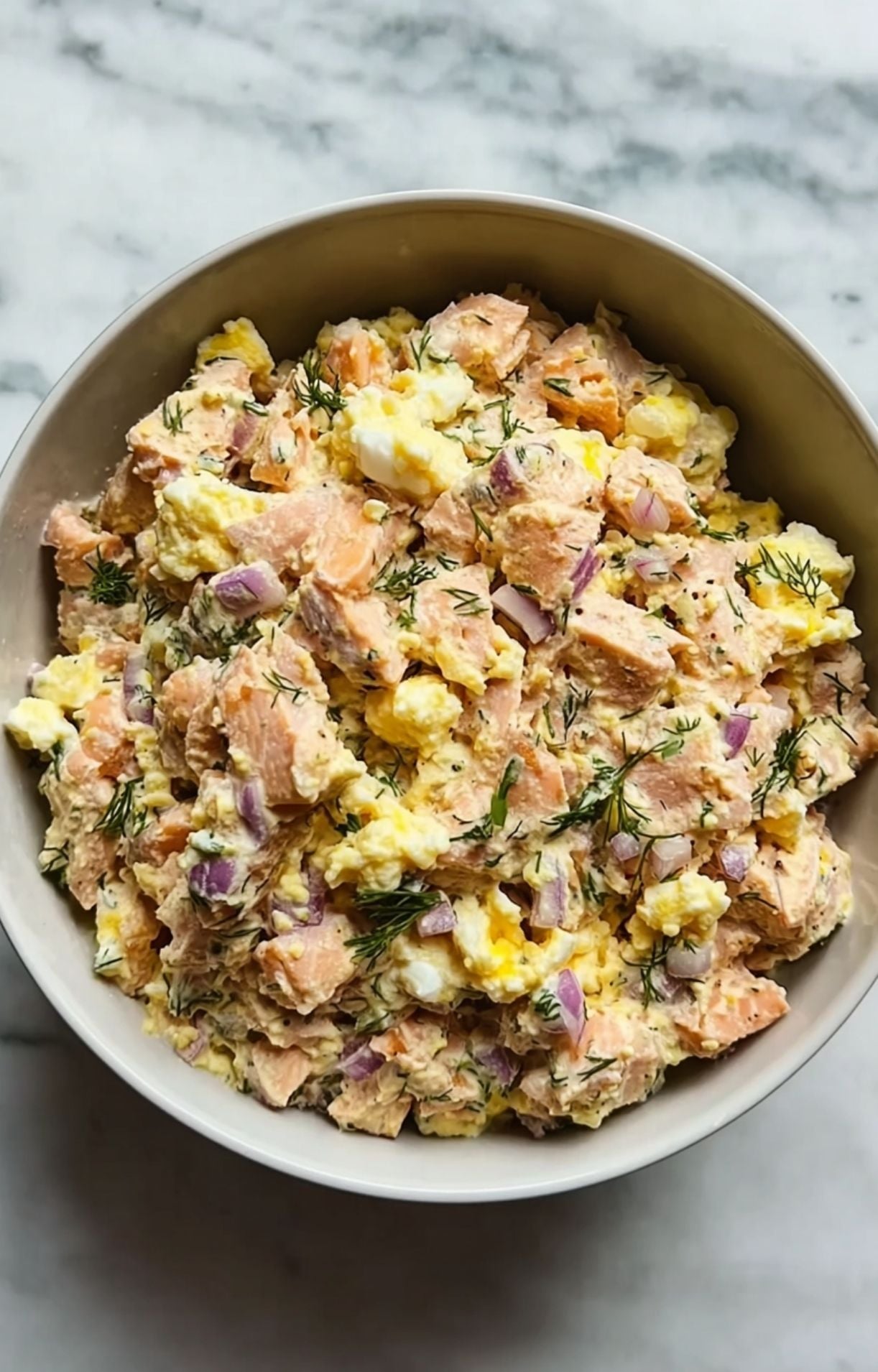 Flaked salmon mixed with eggs, dill, and onions in a bowl, ready to be formed into air fryer salmon patties.