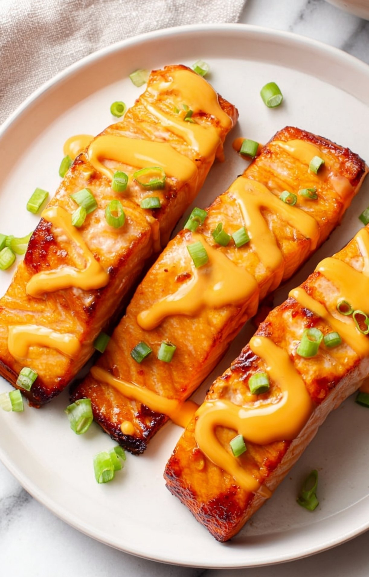 Creamy sauce being drizzled in a zigzag pattern over cooked salmon.
