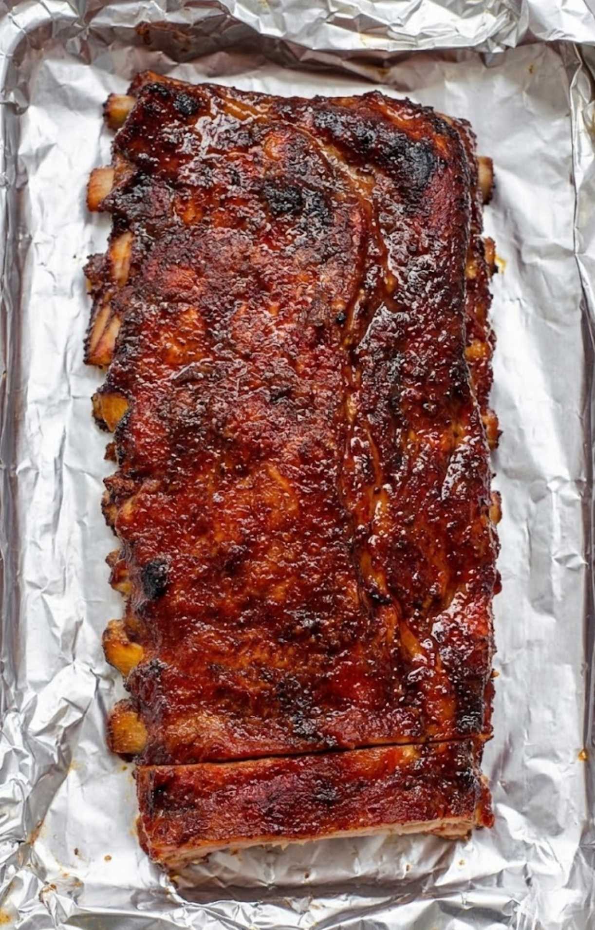 A full rack of smoked ribs glazed with dark BBQ sauce on a foil-lined tray, ready for the final stage of the Pellet Smoker Ribs Recipe.