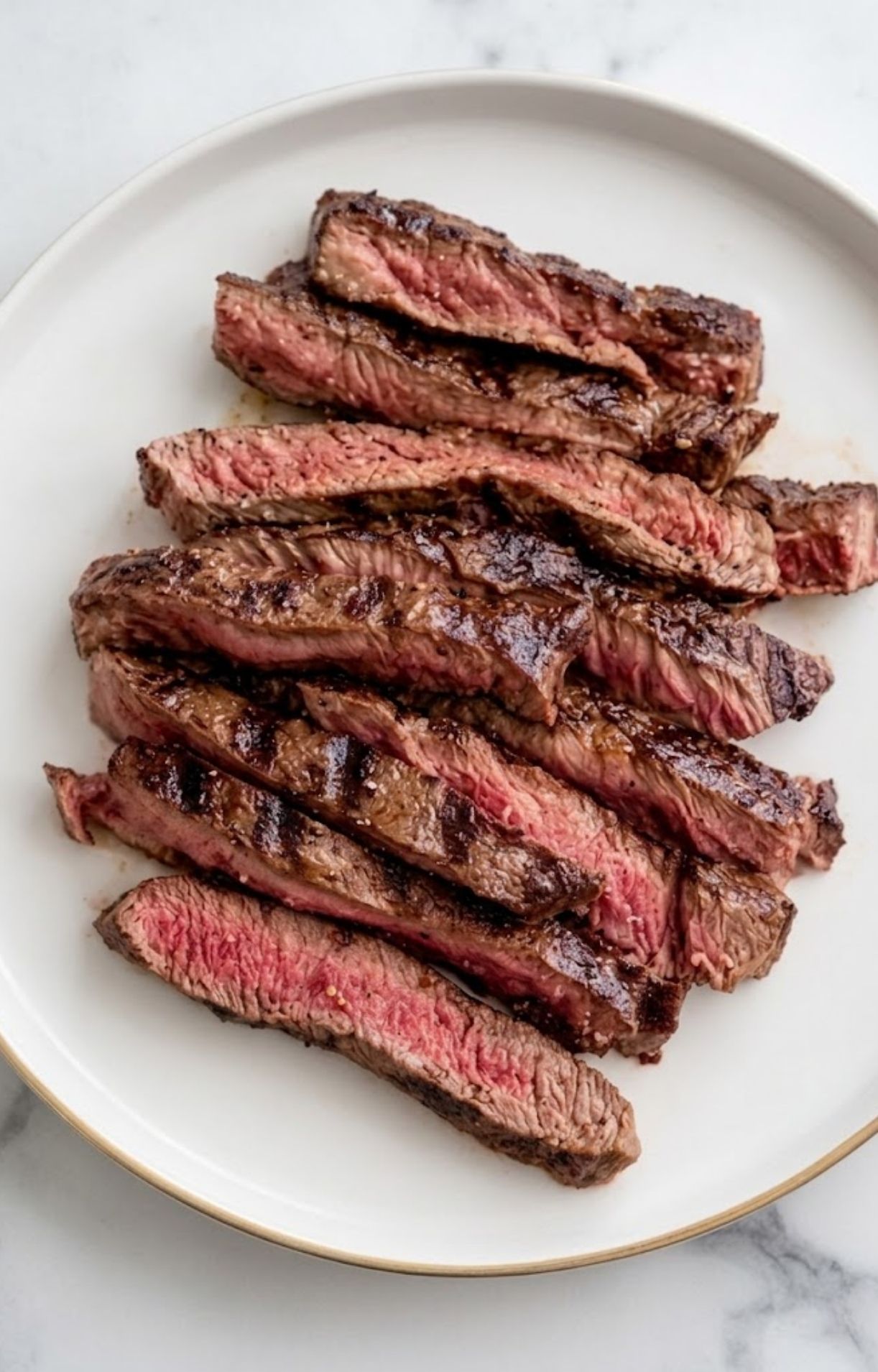 A white plate holding juicy, medium-rare steak strips seasoned and grilled specifically for an Easy Steak Taco Salad Recipe.