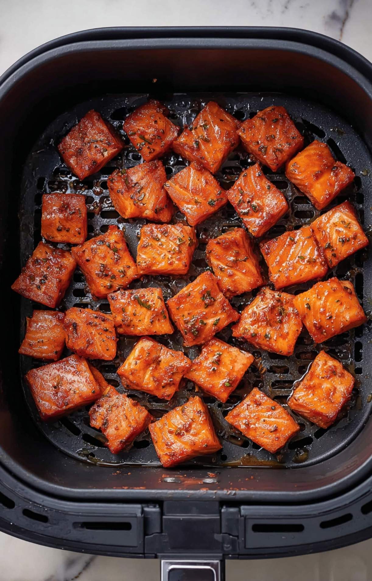 Cubes of seasoned salmon arranged in a single layer inside a black air fryer basket, ready to be cooked into crispy Air Fryer Salmon Bites.