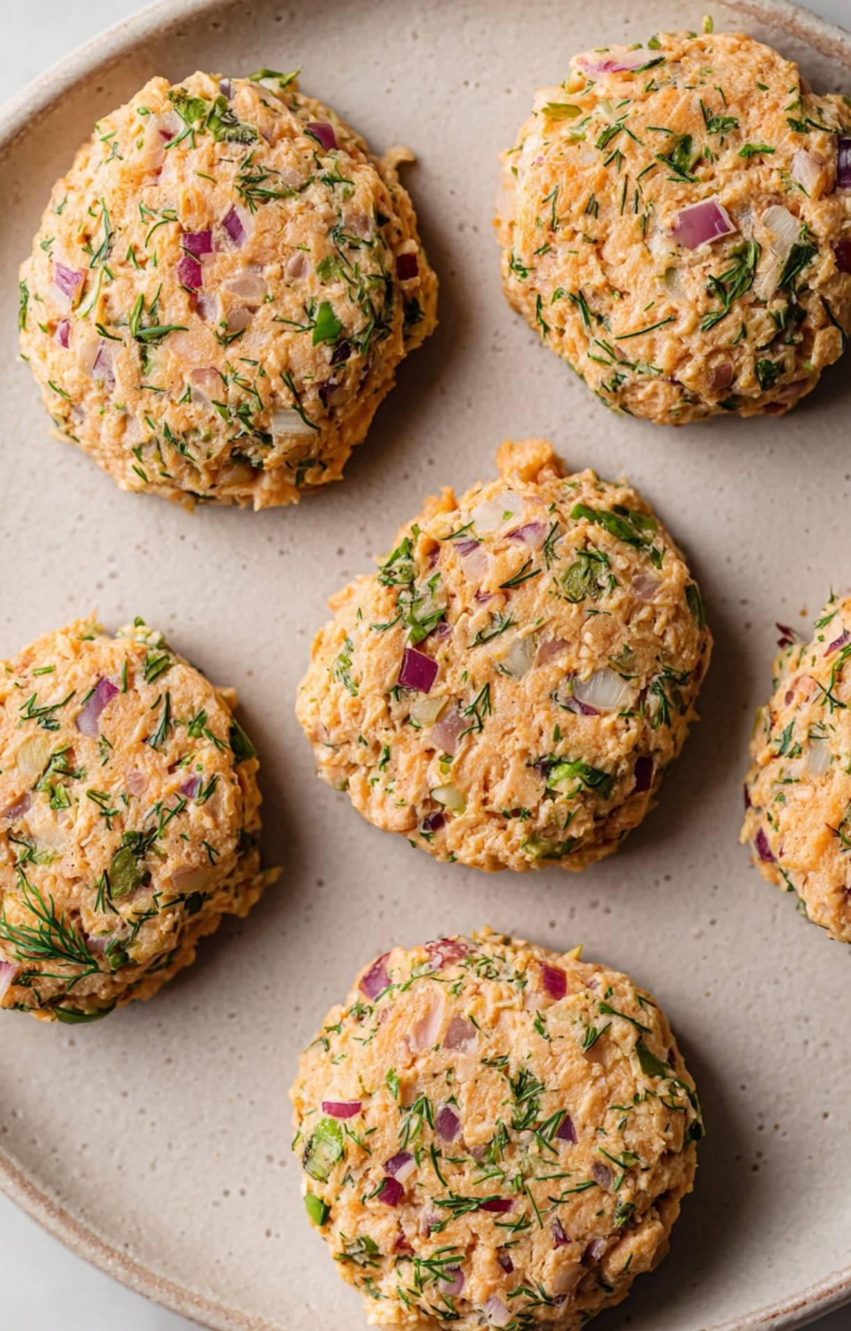 Five uncooked salmon patties formed with fresh dill and red onion, resting on a plate before going into the air fryer.