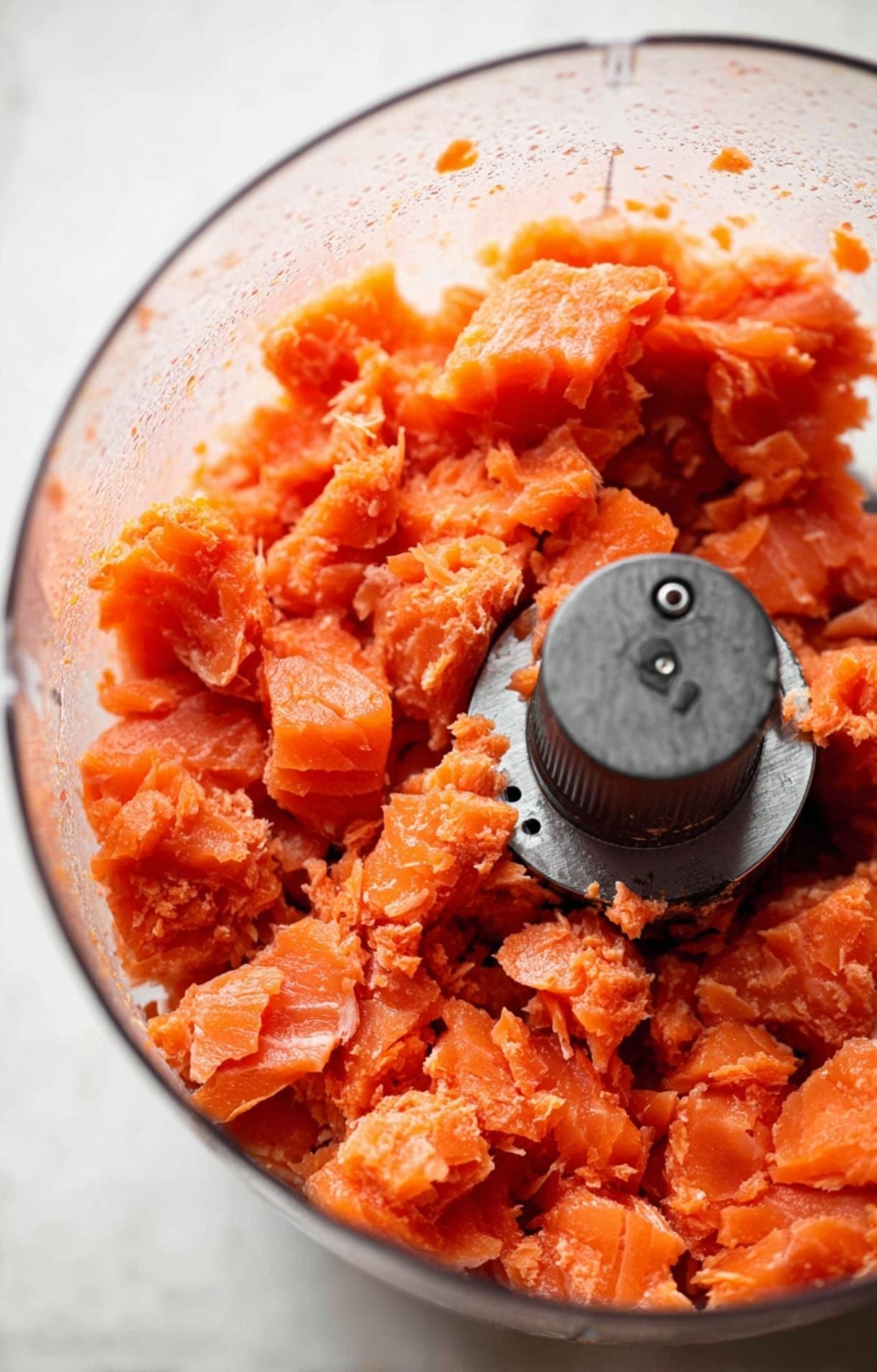 A close-up of fresh, raw salmon being pulsed in a food processor to create a base for the burgers.