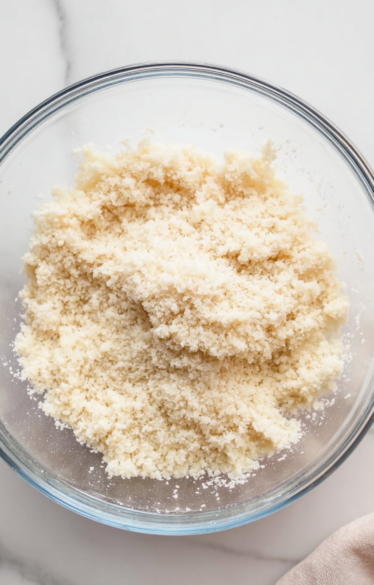 A glass bowl containing a fine, crumbly breadcrumb and cheese mixture used to bind the meatballs.