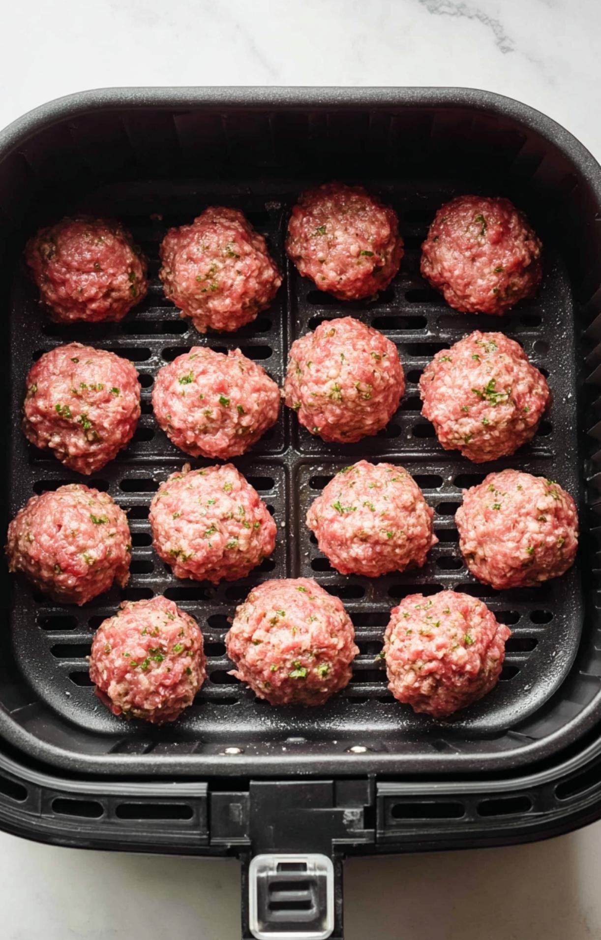 Raw lamb meatballs arranged in a single layer in a black air fryer basket before cooking.